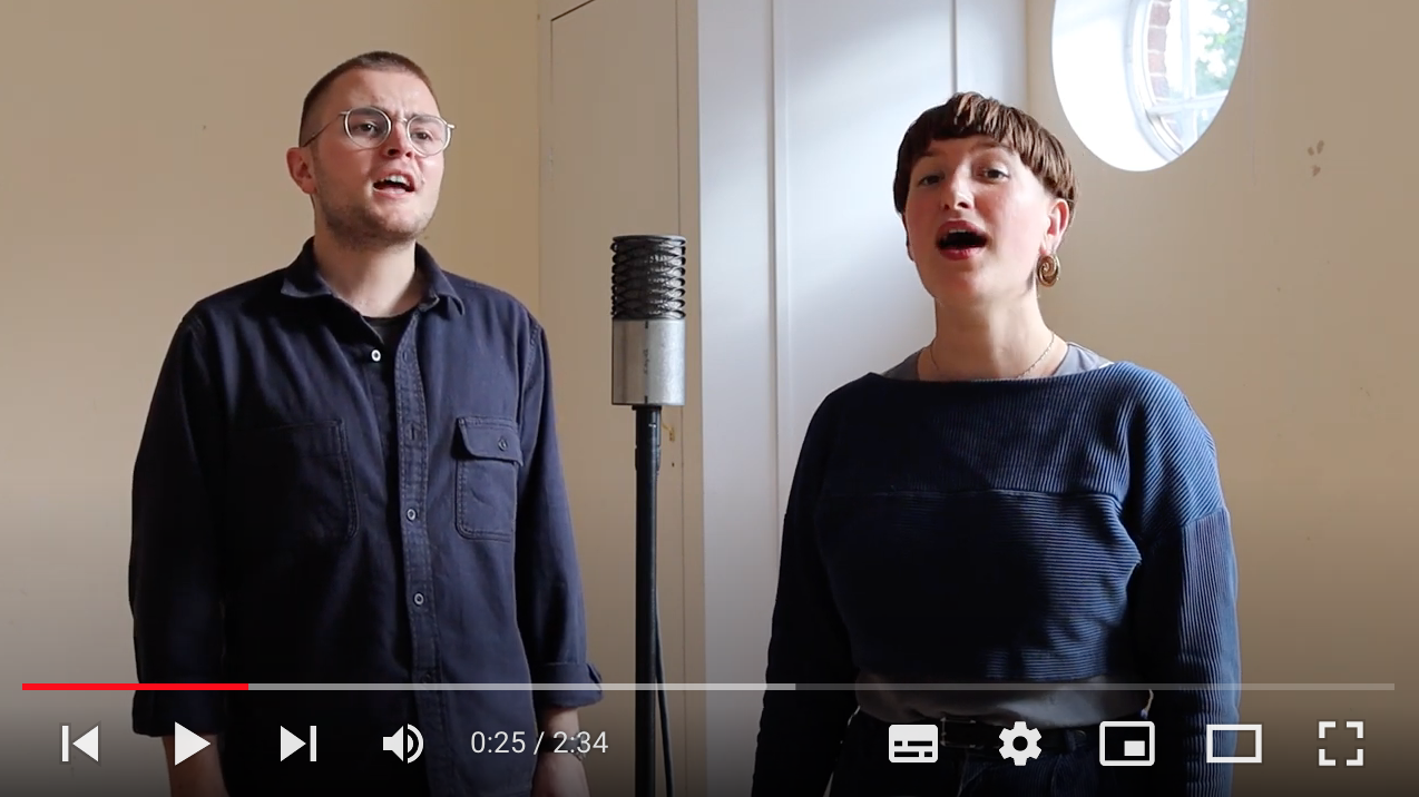 Queer Folk artists George and Sophie singing into a microphone 